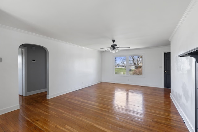 unfurnished living room with baseboards, arched walkways, ornamental molding, ceiling fan, and wood-type flooring