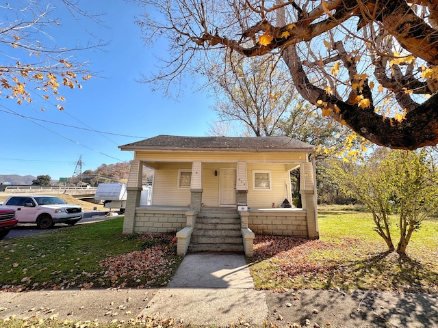 bungalow-style house with a front lawn, covered porch, and a shingled roof