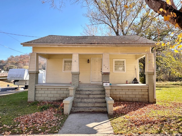 bungalow-style home with covered porch, a front yard, and a shingled roof