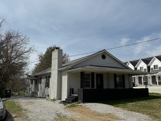view of front facade featuring entry steps, a porch, brick siding, and a chimney