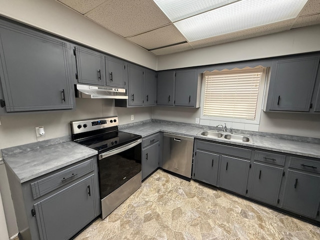kitchen featuring a drop ceiling, gray cabinetry, a sink, under cabinet range hood, and appliances with stainless steel finishes