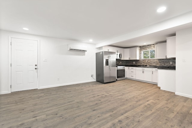 kitchen with light wood-style flooring, appliances with stainless steel finishes, dark countertops, a wall mounted air conditioner, and backsplash