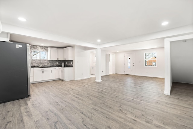 unfurnished living room featuring recessed lighting, light wood finished floors, baseboards, and a sink