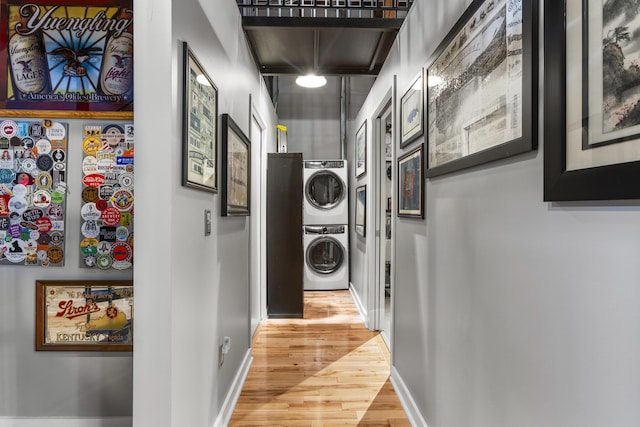 washroom featuring baseboards, light wood-type flooring, stacked washer and clothes dryer, and laundry area