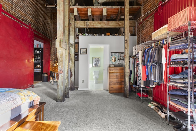 carpeted bedroom with ensuite bathroom, a high ceiling, and brick wall