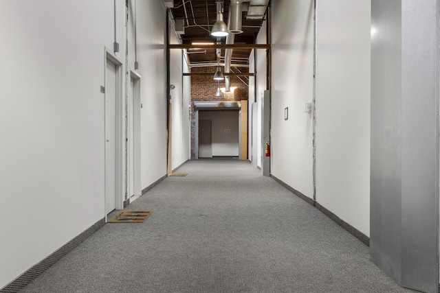 corridor featuring carpet flooring, brick wall, baseboards, and a high ceiling