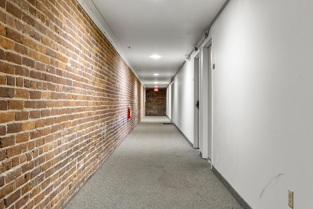 hall featuring light carpet and brick wall