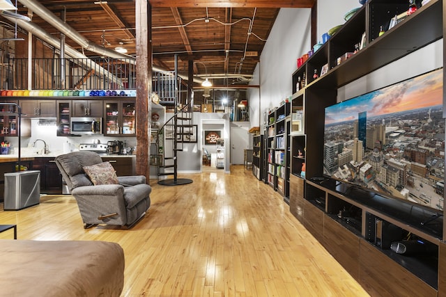 living area with wood ceiling, stairway, a high ceiling, light wood-style flooring, and indoor wet bar