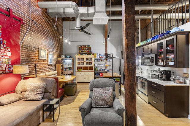 interior space with a high ceiling, light wood-style flooring, dark brown cabinets, appliances with stainless steel finishes, and glass insert cabinets