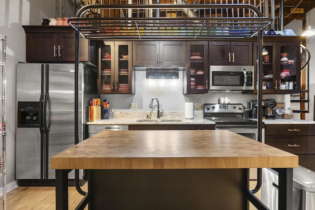 kitchen with a sink, glass insert cabinets, light wood-type flooring, stainless steel appliances, and dark brown cabinets
