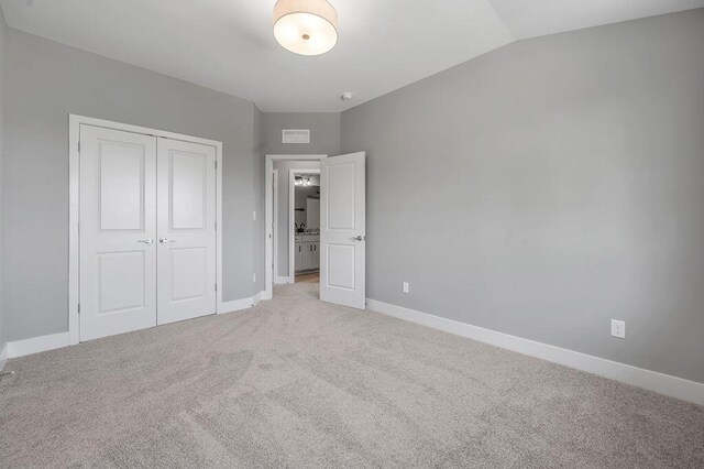 unfurnished bedroom featuring baseboards, vaulted ceiling, light carpet, and a closet