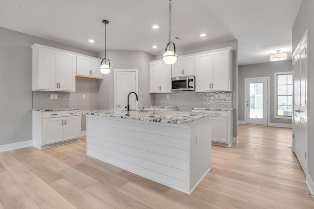 kitchen with a sink, light wood-style floors, decorative backsplash, and stainless steel microwave