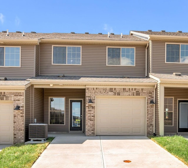 townhome / multi-family property featuring a shingled roof, brick siding, a garage, central AC unit, and concrete driveway