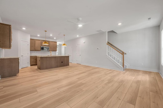 kitchen featuring light wood-style floors, stainless steel microwave, backsplash, visible vents, and a center island with sink