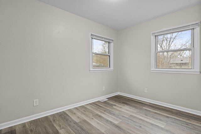 empty room with baseboards, visible vents, and wood finished floors