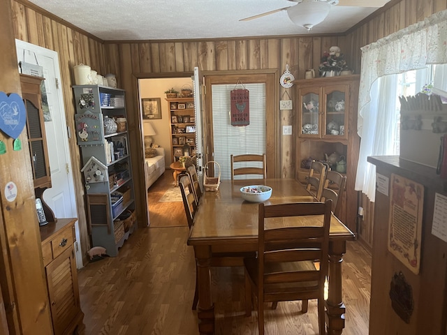 dining room with wood walls, ornamental molding, wood finished floors, a textured ceiling, and a ceiling fan