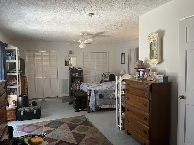 carpeted bedroom with a ceiling fan, visible vents, two closets, and a textured ceiling