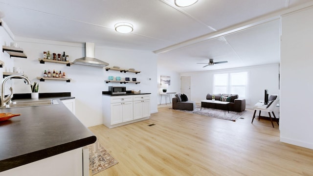 kitchen with a sink, open shelves, stainless steel microwave, wall chimney range hood, and dark countertops