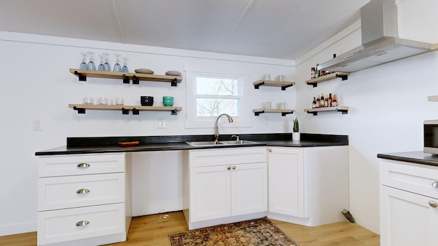 kitchen featuring wall chimney range hood, a sink, dark countertops, and open shelves