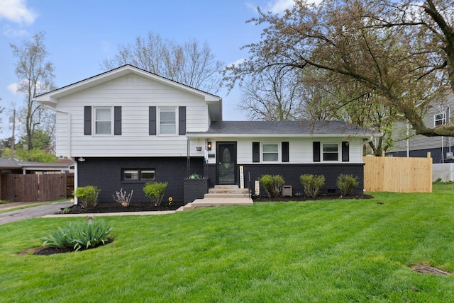 tri-level home with fence, a front lawn, and brick siding