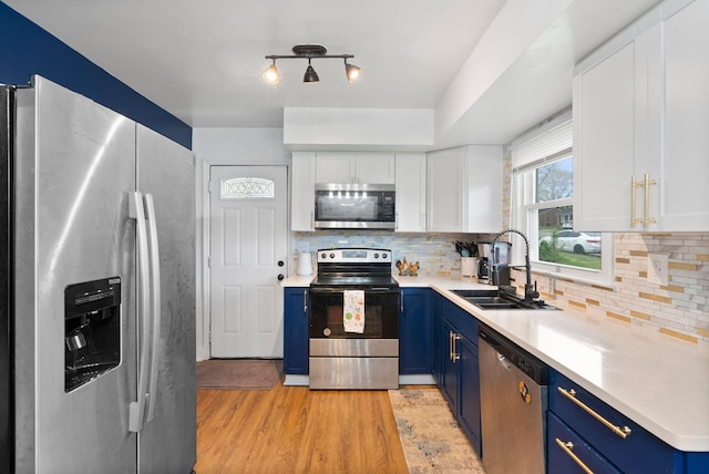 kitchen with white cabinets, blue cabinets, light countertops, a sink, and stainless steel appliances