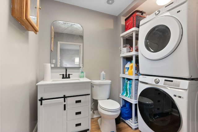 half bath featuring stacked washing maching and dryer, vanity, toilet, and wood finished floors