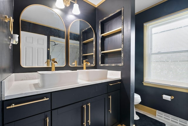 full bathroom with a sink, toilet, double vanity, and baseboards