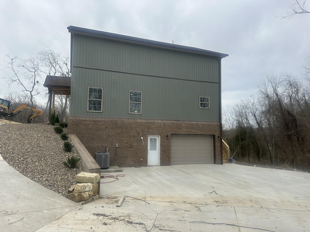view of side of property with central air condition unit, an attached garage, concrete driveway, and brick siding