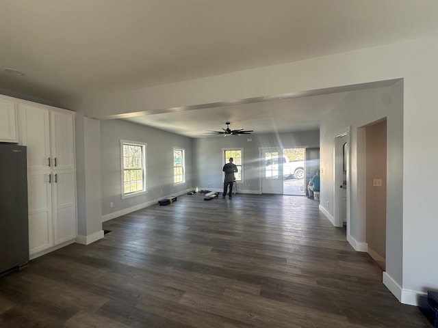 unfurnished living room featuring baseboards, dark wood finished floors, and ceiling fan
