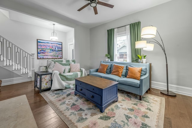 living area with wood-type flooring, baseboards, a ceiling fan, and stairs