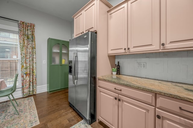 kitchen featuring baseboards, light stone counters, stainless steel fridge, backsplash, and dark wood finished floors