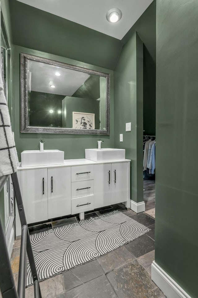 full bath with a sink, stone tile flooring, baseboards, and double vanity