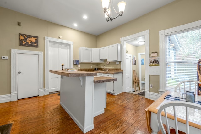 kitchen featuring white cabinetry, wood-type flooring, a sink, a breakfast bar area, and a notable chandelier
