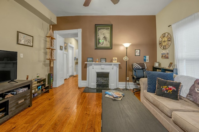 living area with a fireplace with flush hearth, light wood-style flooring, baseboards, and a ceiling fan