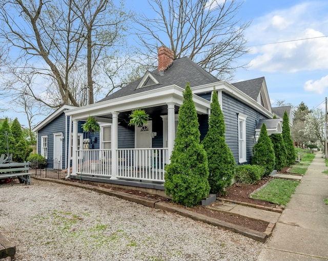 view of front of home featuring a chimney, covered porch, and roof with shingles