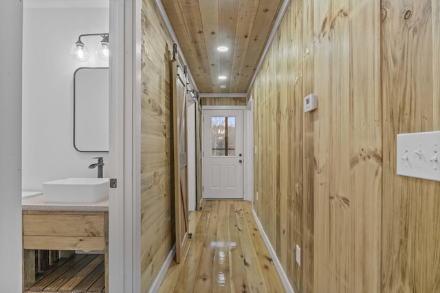 corridor with hardwood / wood-style floors, a sink, wood ceiling, and wooden walls