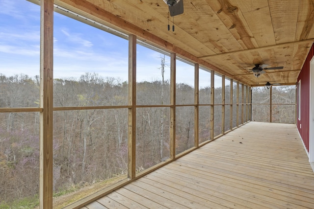 unfurnished sunroom featuring a forest view, ceiling fan, wood ceiling, and wood-type flooring