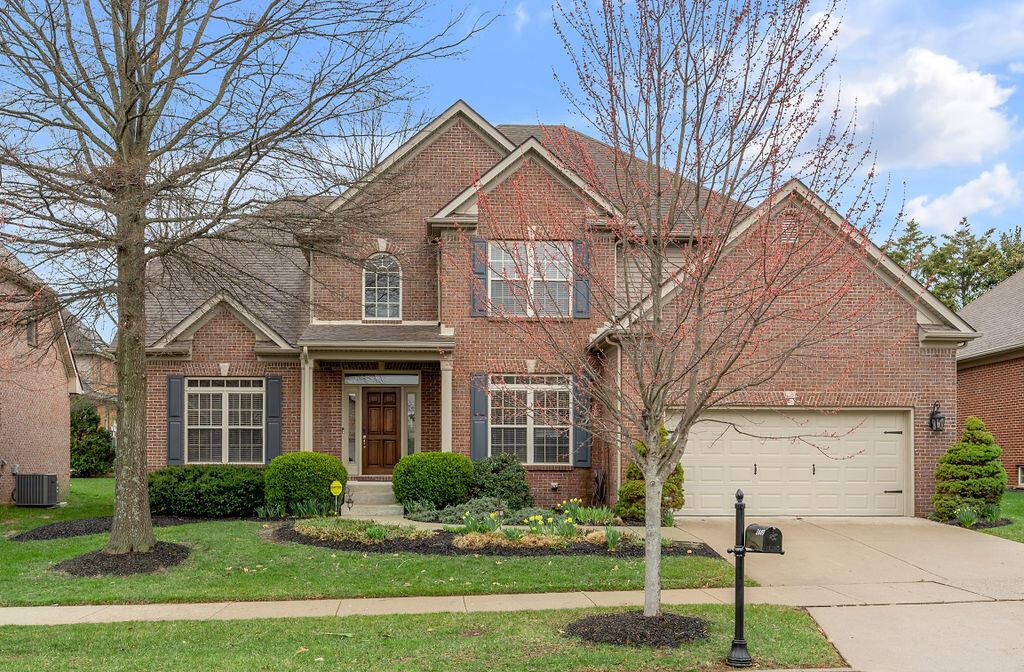 traditional-style home featuring concrete driveway, a front yard, brick siding, and cooling unit