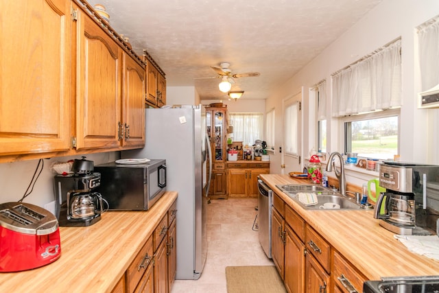 kitchen featuring appliances with stainless steel finishes, butcher block counters, ceiling fan, and a sink