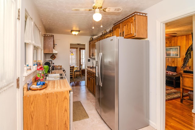 kitchen with a ceiling fan, a sink, brown cabinetry, stainless steel fridge with ice dispenser, and light countertops