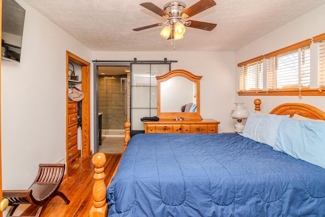 bedroom with a barn door, ceiling fan, a textured ceiling, and wood finished floors