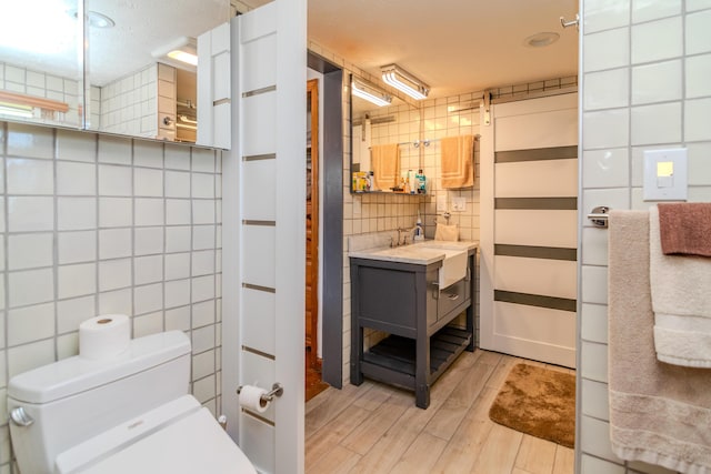 bathroom with tile walls, toilet, a sink, wood finished floors, and tasteful backsplash