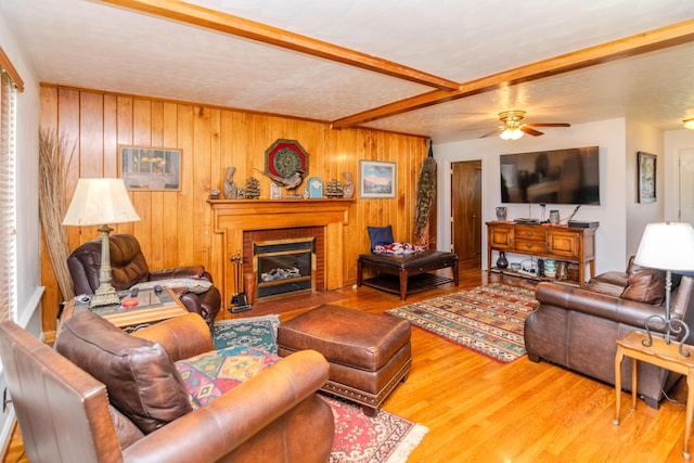 living area with wood walls, beam ceiling, ceiling fan, and wood finished floors