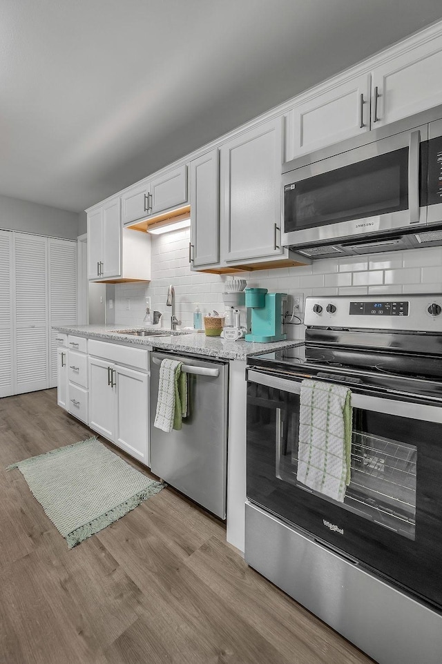 kitchen with a sink, tasteful backsplash, appliances with stainless steel finishes, white cabinets, and light wood-style floors