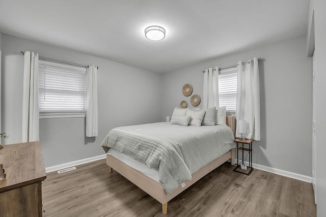 bedroom with baseboards, visible vents, and wood finished floors