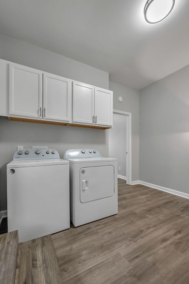 clothes washing area with baseboards, cabinet space, wood finished floors, and separate washer and dryer