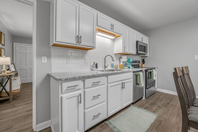 kitchen featuring white cabinetry, backsplash, a sink, appliances with stainless steel finishes, and wood finished floors