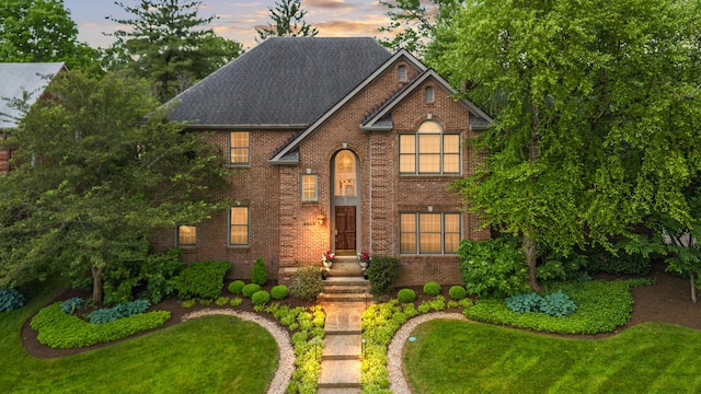 view of front of home featuring brick siding, a front yard, and roof with shingles