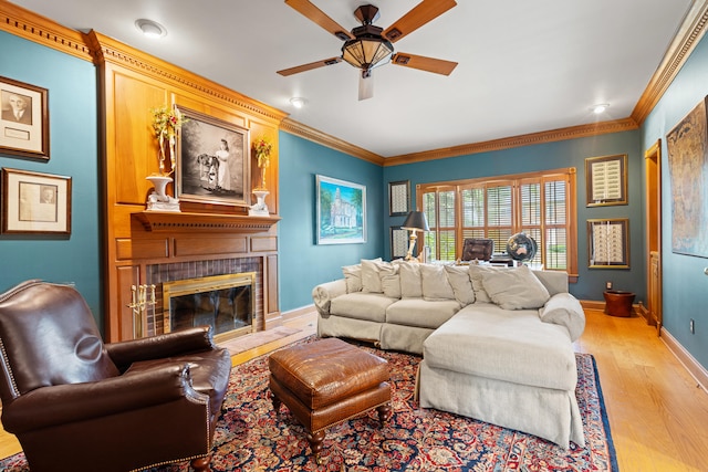 living room with light wood finished floors, a ceiling fan, a fireplace, baseboards, and ornamental molding