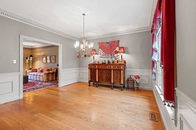 dining area featuring wainscoting, a chandelier, ornamental molding, wood finished floors, and a decorative wall